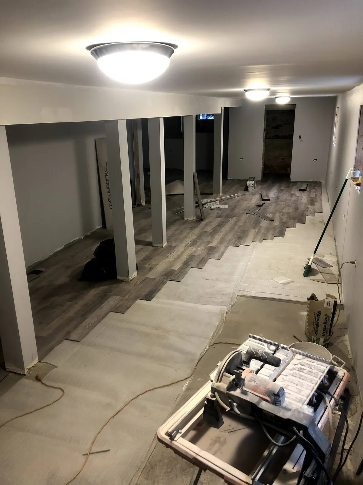Luxury vinyl plank flooring being installed row by row across a lower level